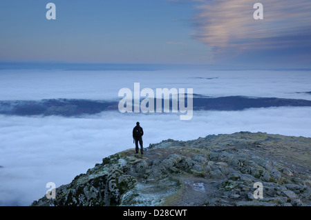 Lone figure above a sea of cloud on the summit of the Old Man of Coniston at dusk in the English Lake District Stock Photo