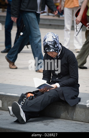 Berlin, Germany, young woman wearing a headscarf sits reading on a step Stock Photo