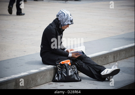 Berlin, Germany, young woman wearing a headscarf sits reading on a step Stock Photo