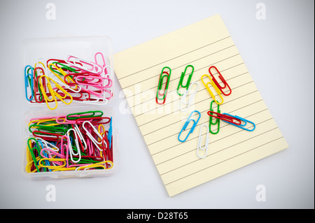 Colorful paper clips on pile of yellow paper against white background Stock Photo