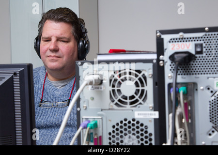 Computer class for people with visual impairments - man using headphones for audio. Stock Photo