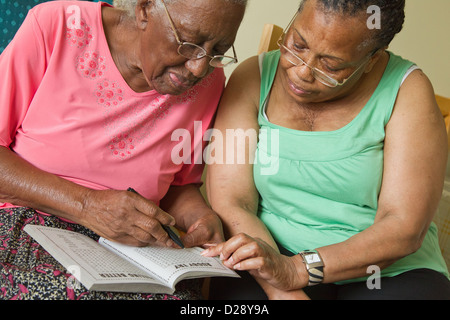 Carer and elderly visually impaired woman solving crossword. Stock Photo