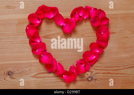 Heart shape made from red rose petals placed upon on a rustic wooden background. Stock Photo