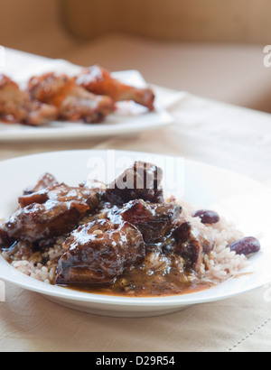 Caribbean style curried Oxtail served with rice mixed with red kidney beans. Backdrop of chicken wings. Shallow DOF. Stock Photo