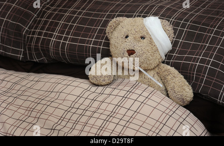 TEDDY BEAR IN BED WITH BANDAGE AND THERMOMETER RE ILLNESS MAN FLU SICKNESS THROWING A SICKIE TIME OFF WORK WORKERS DAY WELL UK Stock Photo