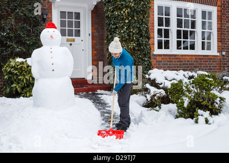 Woman shovels snow outside her home in UK Stock Photo