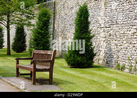 Wooden bench in a formal garden next to an ancient Roman wall in Winchester, UK Stock Photo