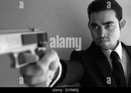 An Asian guy in a suit brandishing a handgun in black and white. A man holding a gun. Stock Photo