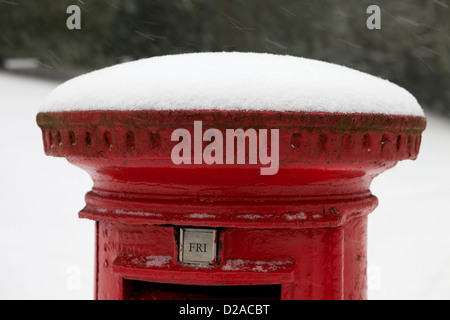 Royal Mail traditional red post box standing in the snow, with snow covering the top Stock Photo