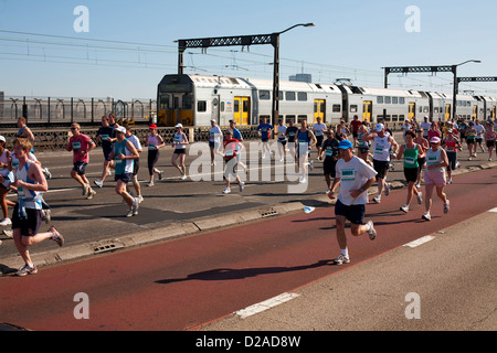 Fitness enthusiasts on Charity fun run running across the Sydney Harbour Bridge with suburban train passing them. Stock Photo