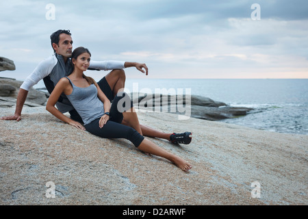 Couple relaxing on boulder by ocean Stock Photo