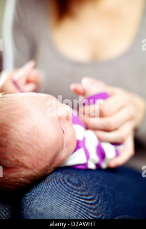 Young mother playing with her tiny baby holding its hands as it lies on her lap Stock Photo
