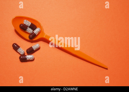 orange plastic spoons with color pills on orange background Stock Photo