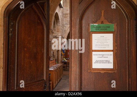 Close-up of welcome sign on wooden doors (1 open & one closed) from porch to nave - interior of Church of Saint Mary, Masham, Yorkshire, England, UK. Stock Photo