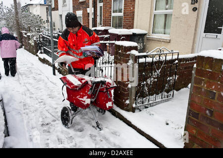Royal Mail postman delivers mail in snowy winter weather, while an elderly lady treads through the icy conditions underfoot. Reading, Berkshire, England, UK. Stock Photo