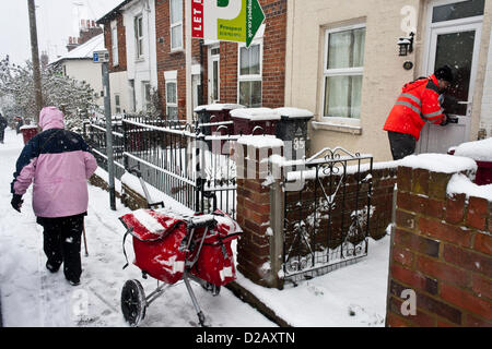 Royal Mail postman delivers mail in snowy winter weather, while an elderly lady treads through the icy conditions underfoot. Reading, Berkshire, England, UK. Stock Photo