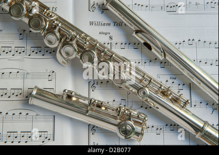 Close-up, partial view of dismantled parts of musical instrument (flute head, body, foot joint) laying on open music book - Yorkshire, England, UK. Stock Photo