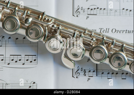 Close-up partial view of musical wind instrument (flute body joint) laid on open pages of music book (William Tell Overture) - Yorkshire, England, UK. Stock Photo