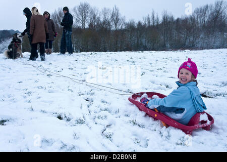 Girl celebrates her birthday sledging on a hill in Reading suburb, Woodley, Berkshire.  Her dog, an Alaskan Malamute, waits to pull her along, while dad chats with others. Stock Photo