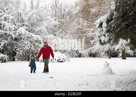 Man and child holding hands walking in snow in public park with snowman, Sophia Gardens, Abergavenny, Wales, UK Stock Photo