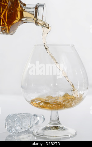 High speed frozen stream decanting cognac poured into a brandy snifter on white background Stock Photo