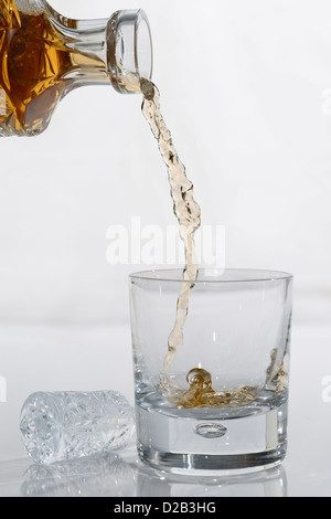 Pouring Whiskey from a crystal decanter into a tumbler glass on white background Stock Photo