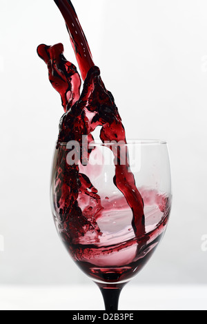 Complex frozen splash pattern of red wine poured into glass stemware on a white background High speed frozen stream Stock Photo