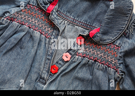 red and pink daisy flower shaped buttons and smocking on little girl's denim smock dress Stock Photo