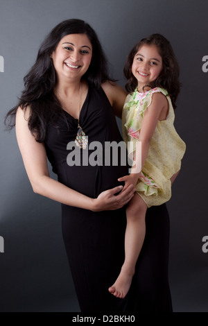 Portrait of a smiling, pregnant East Indian woman sitting with her daughter. The woman is wearing a formal gown. Stock Photo