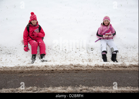 Young schoolgirls sitting on the roadside after a heavy fall of snow rural location in Hampshire England UK Stock Photo