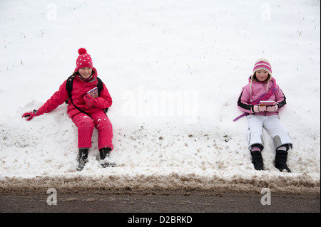 Young schoolgirls sitting on the roadside after a heavy fall of snow rural location in Hampshire England UK Stock Photo