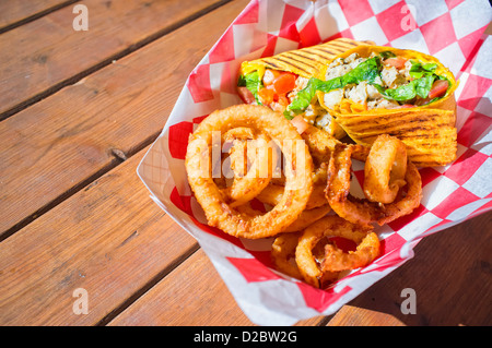 Close up of fast food meal of chicken meat wrap and fried onion rings served in paper container Stock Photo