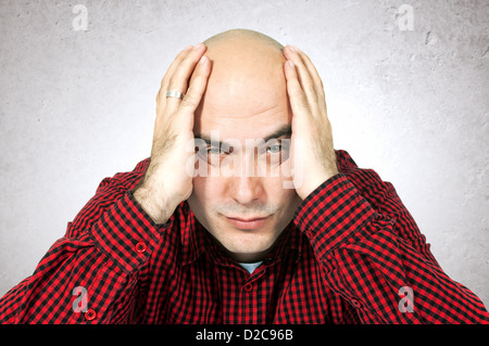 Worried young adult bald man sitting at the table with hands on his head. Stock Photo