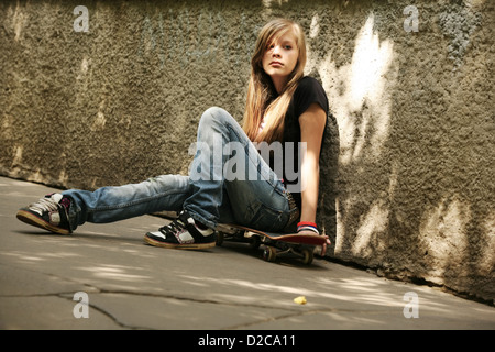 The girl with skateboard sitting against a wall Stock Photo