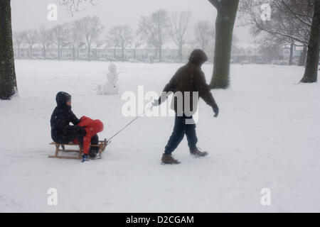 A family out in the snow enjoy a winter's day with their child and sledge in a snowbound south London park. During a prolonged cold spell of bad weather, snow fell continuously on the capital on Sunday, allowing families the chance to enjoy the bleak conditions, here in Ruskin Park in the borough of Lambeth. Pulling the mother and a young child who are riding on the sledge, the man walks through powder on a freezing day where snow is still falling. A primitively-built snowman stands in the background while further down the hill are Edwardian period homes beneath 100 year-old ash trees. Stock Photo