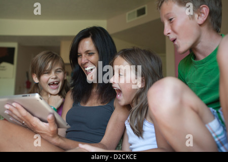 Mother and her three kids looking at an ipad tablet together and laughing at home. Stock Photo