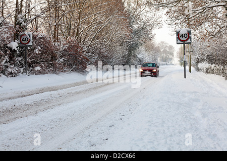 A red car travels along a snow covered road in Devon, UK Stock Photo