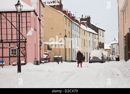 A woman in a red hat and fur coat walks past historic buildings in the snow Stock Photo