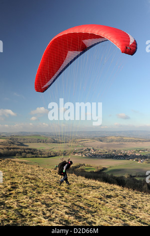 A male  paraglider takes off over the South Downs in West Sussex with a red chute on a fine day with blue sky and white clouds Stock Photo