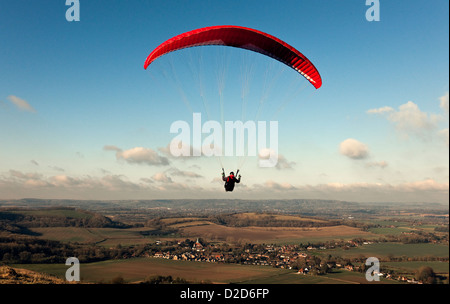 A para-glider flies over the South Downs in West Sussex with a red chute on a fine day with blue sky and white clouds Stock Photo