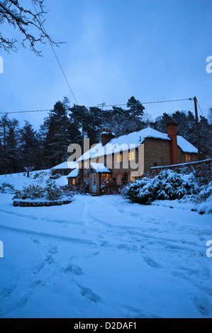 Christmas card image of a snowy cottage at night with all the lights on and tracks in the snow in winter Stock Photo