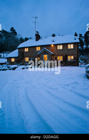 Christmas card image of a snowy cottage at night with all the lights on and tracks in the snow Stock Photo