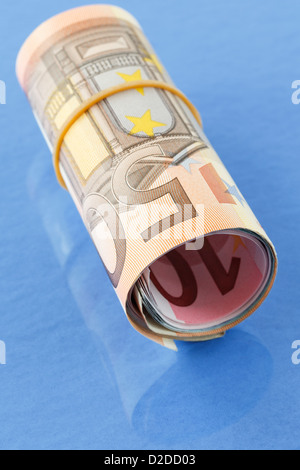 50 Euro notes in a roll of Euros rolled up with an elastic band on a plain blue background Stock Photo