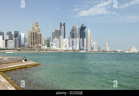 A lone fisherman tries his luck on the doha corniche in Qatar with the bulk of the city's new high-rise skyline behind Stock Photo