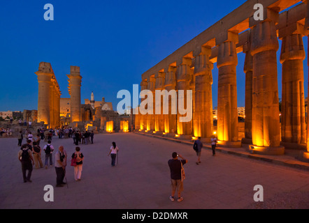 Tourists walking among the Floodlit columns of the court of Amenhotep III  Temple of Luxor at sunset Luxor Egypt Middle East Stock Photo