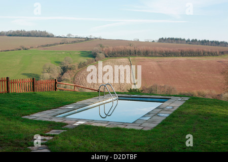 Outdoor swimming pool overlooking a beautiful view in Ashcombe, Devon, England. Sunshine and blue sky reflected in the water. Stock Photo