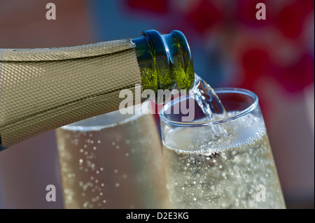 Pouring sparkling chilled glasses of sparkling wine champagne on sunlit terrace with colourful Bougainvillea flowers and lifestyle pool in background Stock Photo