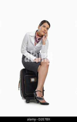 Air hostess sitting on her luggage and thinking Stock Photo