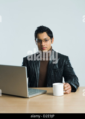 Man working on a laptop and drinking a cup of coffee Stock Photo