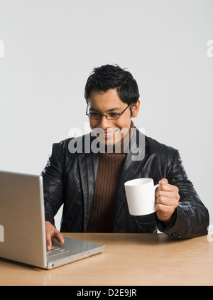Man working on a laptop and drinking a cup of coffee Stock Photo